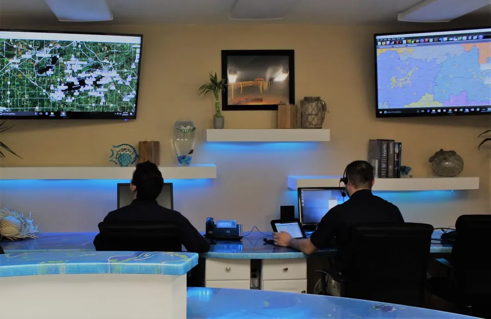 Poolblu team members at a dispatch desk with service-territory maps on wall screens.