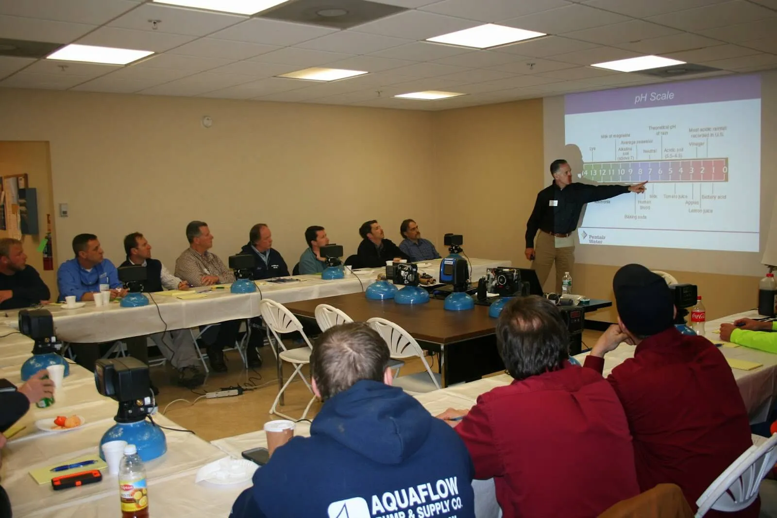 An instructor leads a Poolblu Training Institute class with a water-chemistry slide on screen.